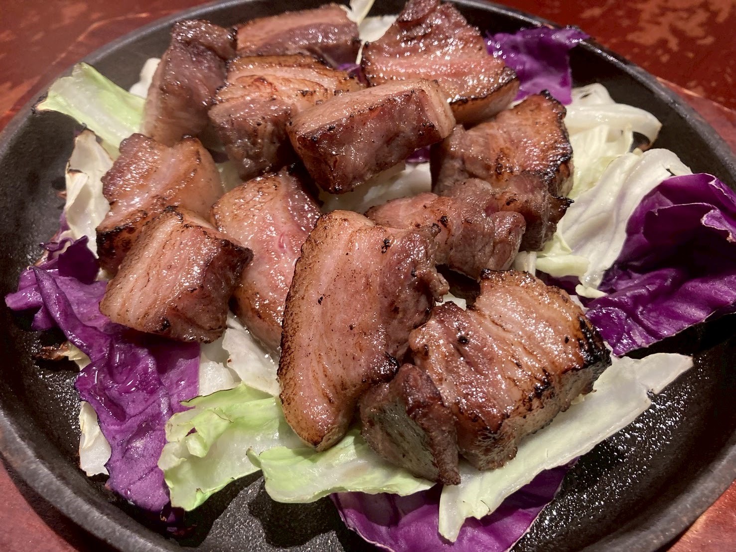 紫と白のキャベツを敷いた黒い皿に、焼き目の濃い角切りの肉。