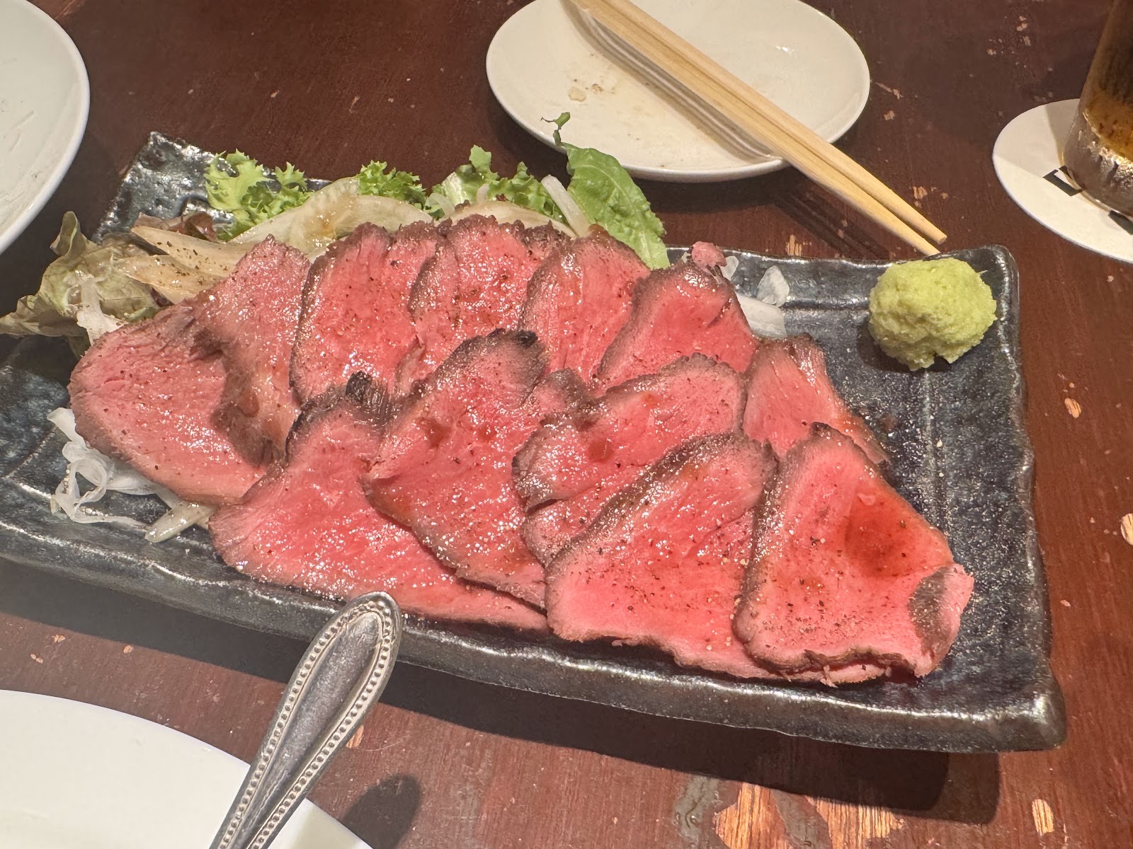 黒い長皿に扇状に並べた、表面を焼いた赤身肉の薄切り。山葵を添えて。