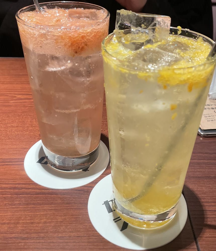 金属のストローを挿した背の高いグラスのサワー2杯。ピンク色のものと、柑橘の皮が浮いた黄色いもの。