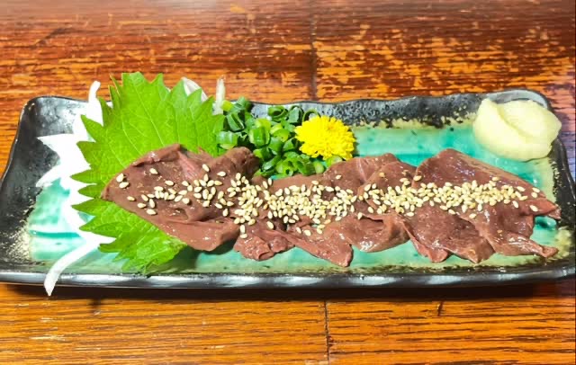 青緑の長皿に大葉を敷き、ごまをふった濃い赤色の刺身。黄色い菊と薬味を添えて。