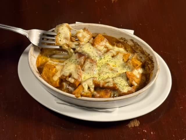 白い耐熱皿にチーズを焼き付けたグラタン。フォークで一口すくっている。