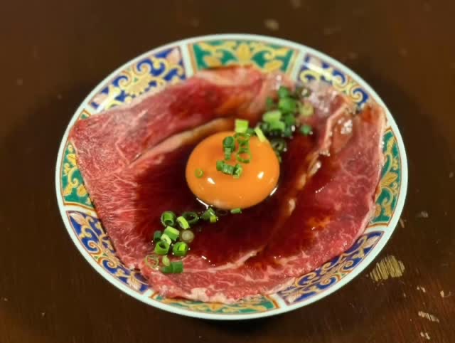 色絵の皿に薄切りの炙り肉を敷き、中央に卵黄と刻みねぎ。