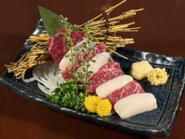 黒い皿に赤身と白い脂身の刺身を交互に並べ、大根のつまと黄色い菊、薬味二種を添えて。