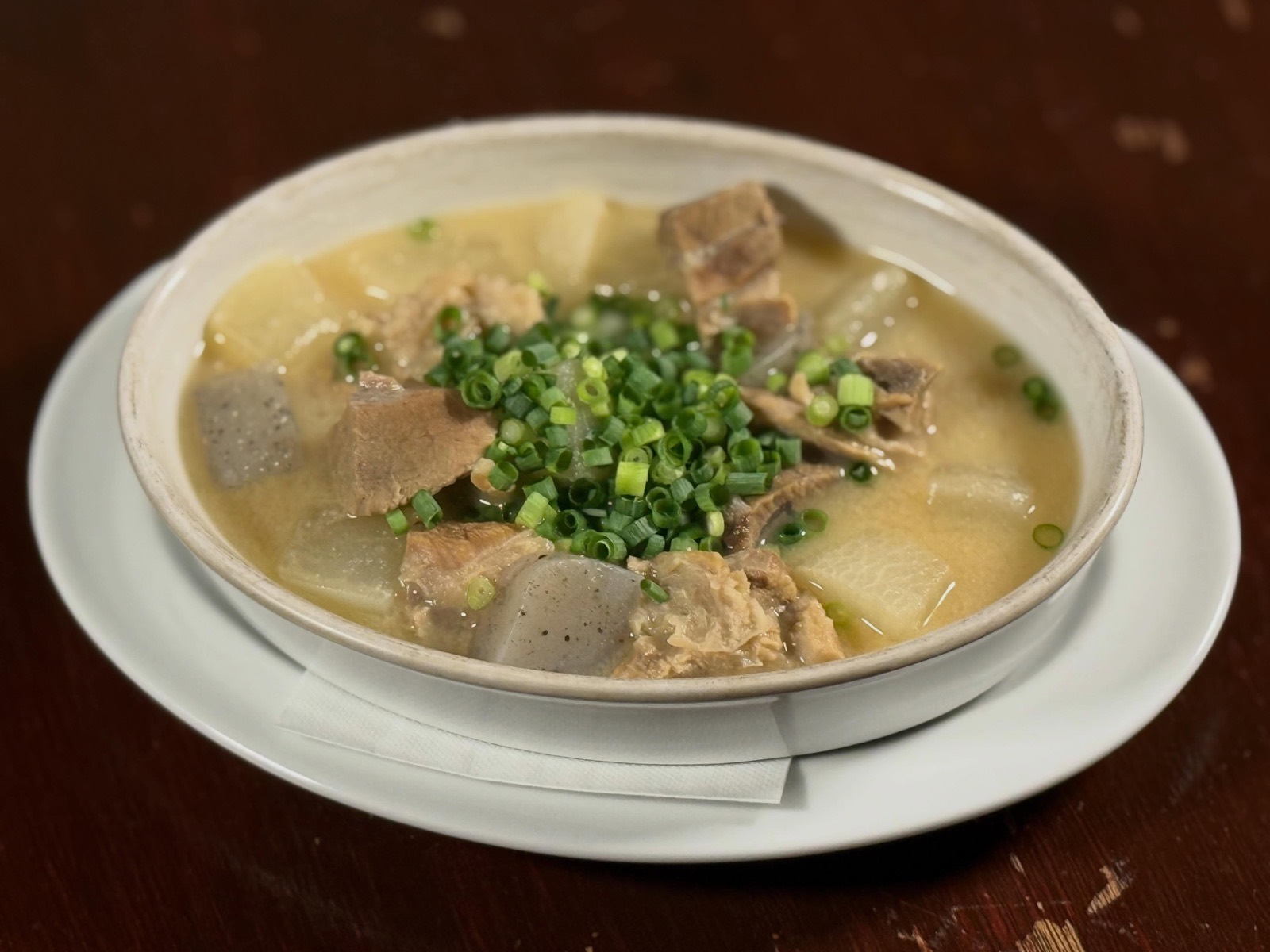 白い器に、大根とこんにゃくと肉を煮込んだ薄茶色の汁物。たっぷりの刻みねぎをのせて。